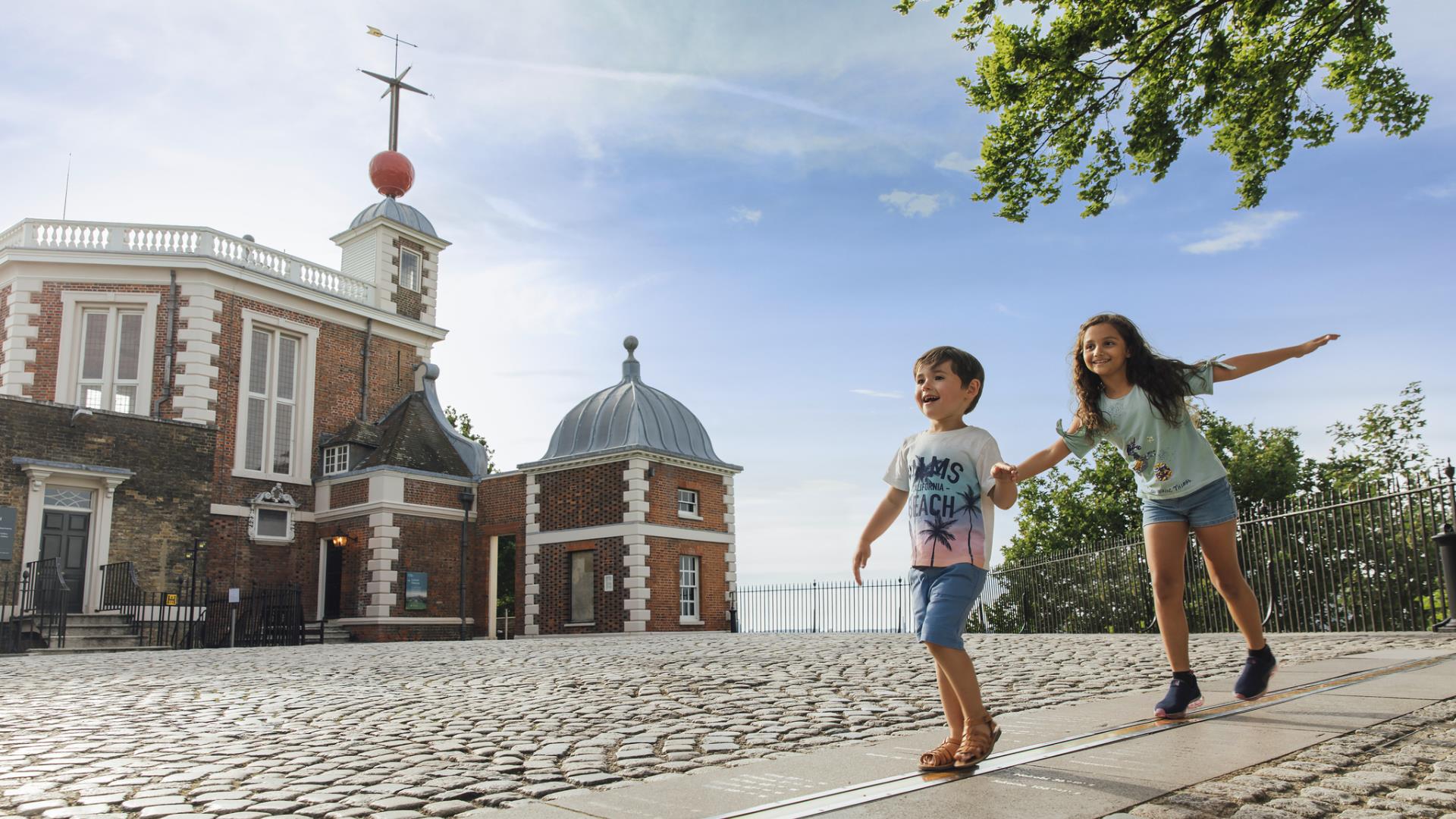 A boy and a girl walk along the Meridian Line in the courtyard of the Royal Observatory in Greenwich.
