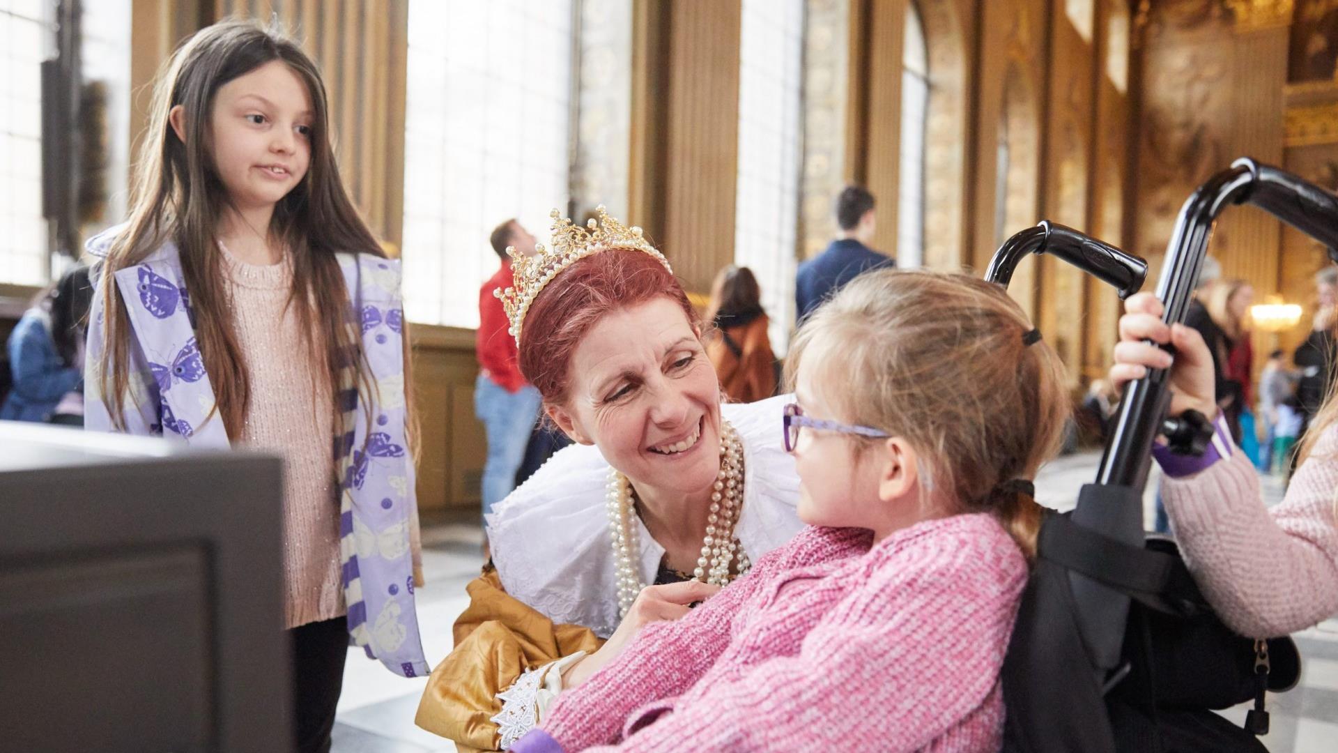 A young girl in a wheelchair is greeted by staff at the Painted Hall at the Old Royal Naval College in Greenwich.