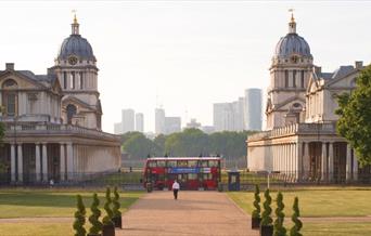 A London Bus centre aligned between Old Royal Naval College domes in Greenwich looking toward the river Thames in Greenwich