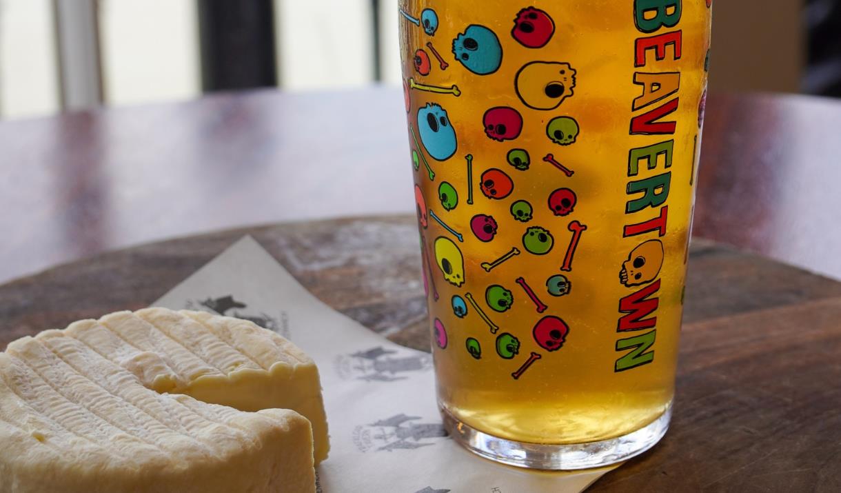 A glass of Beavertown beer and a round cheese.