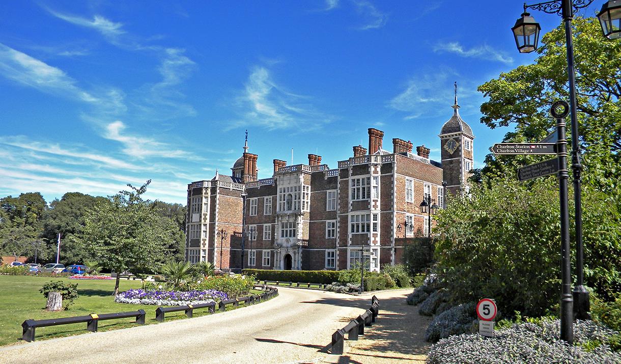 The front of Charlton House on a sunny summer's day surrounded by lush green grass and flowers.