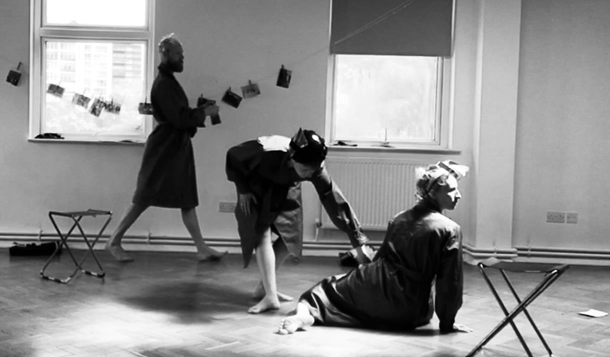 Three dancers in dressing gowns rehearsing in an almost empty room.