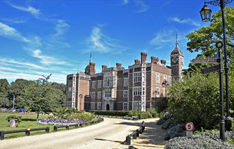 The front of Charlton House on a sunny summer's day surrounded by lush green grass and flowers.