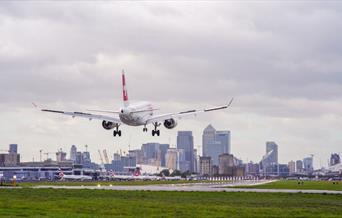 A plane comes in to land at London City Airport with Canary Wharf in the background.