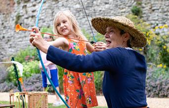 Join Eltham Palace every day of the summer holidays to learn what life was like in medieval times - woman in medieval costume helping a girl with a bo