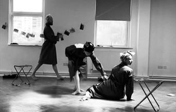 Three dancers in dressing gowns rehearsing in an almost empty room.